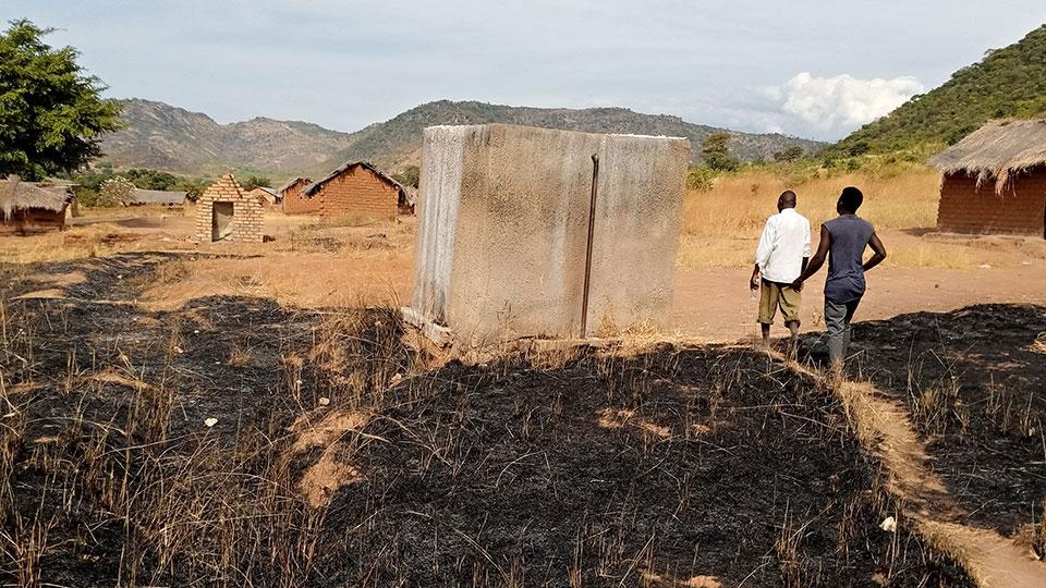 Two people walk past non-functional water storage tank at Wampembe village in Rukwa region, Tanzania